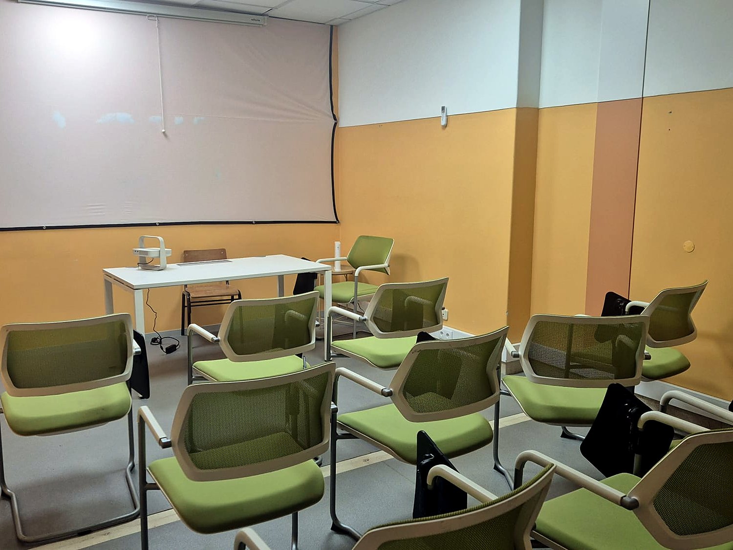Sala de formação com ecrã de projecção e cadeiras com palmatória